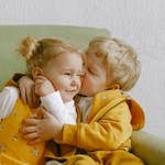 Cheerful little siblings hugging in armchair at home